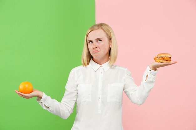 Diät. Diätkonzept. Gesundes Essen. Schöne junge Frau, die zwischen Früchten und unhelathischem Fast Food wählt