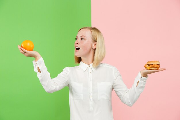 Diät. Diätkonzept. Gesundes Essen. Schöne junge Frau, die zwischen Früchten und unhelathischem Fast Food wählt