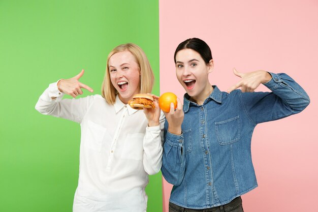 Diät. Diätkonzept. Gesundes nützliches Essen. Schöne junge Frauen, die im Studio zwischen Früchten und unhelathischem Fast Food wählen. Menschliche Emotionen und Vergleichskonzepte