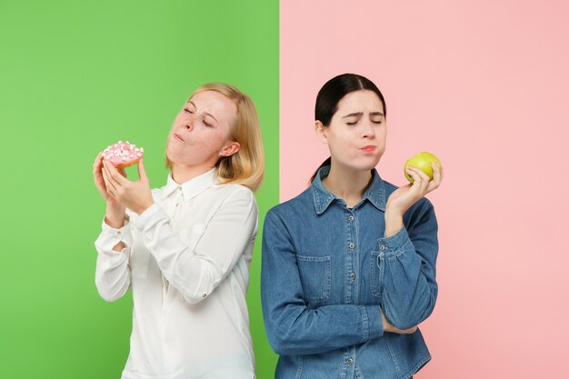 Diät. Diätkonzept. Gesundes nützliches Essen. Schöne junge Frauen, die zwischen Früchten und Unhelathy-Kuchen im Studio wählen. Menschliche Emotionen und Vergleichskonzepte