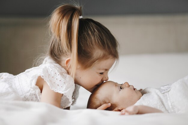 Die ältere Schwester küsst ein kleines Mädchen mit geschlossenen Augen auf die Stirn