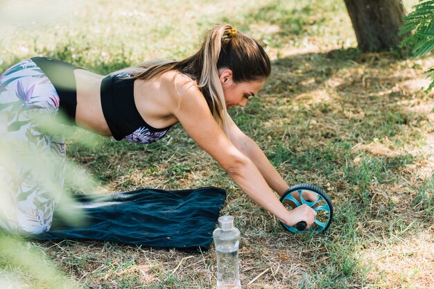 Die aktive sportliche Frau, die Übung mit ABS-Rolle tut, drehen herein Park