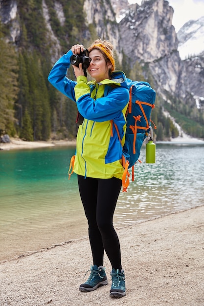 Die aufnahme eines positiven fotografen in voller länge macht ein foto des türkisfarbenen gebirgsflusses und posiert an einem wunderschönen ort für einen touristenbesuch