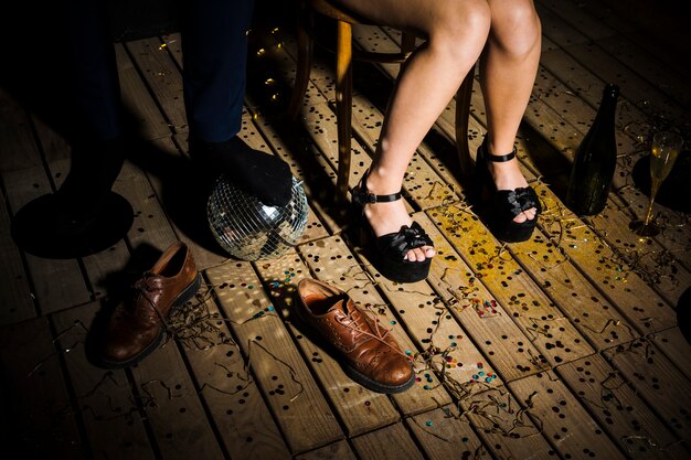 Die Beine der Frau in den Schuhen nähern sich dem Bein des Mannes auf Discoball nahe Stiefeln
