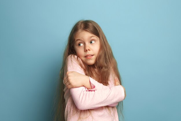 Die Überraschung. Das überraschte jugendlich Mädchen auf einem blauen Studiohintergrund. Gesichtsausdrücke und Menschen Emotionen Konzept. Trendige Farben. Vorderansicht. Porträt in halber Länge