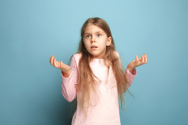 Die Überraschung, Verwirrung, Freude. Das überraschte jugendlich Mädchen auf einem blauen Studiohintergrund. Gesichtsausdrücke und Menschen Emotionen Konzept. Trendige Farben. Vorderansicht. Porträt in halber Länge