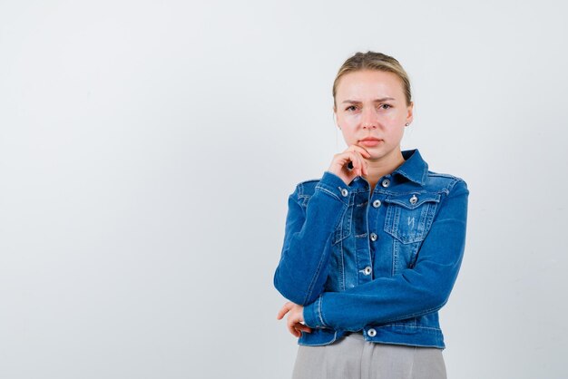 Die blonde Frau denkt, indem sie ihre Hand am Kinn auf weißem Hintergrund hält