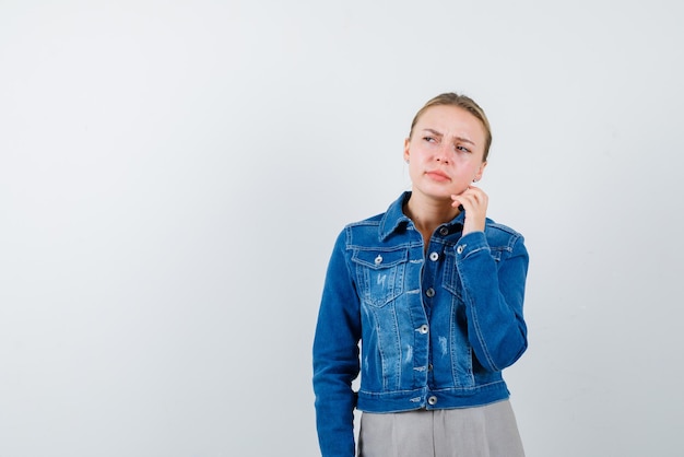 Die blonde Frau denkt nach, indem sie ihre Hand auf die Wange auf weißem Hintergrund hält