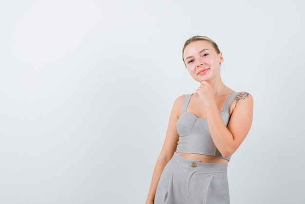 Die blonde Frau lächelt, indem sie ihre Hand am Kinn auf weißem Hintergrund hält