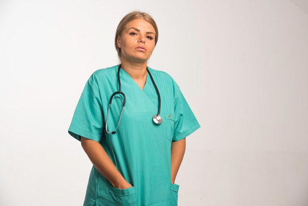 Die blonde Ärztin in blauer Uniform mit Stethoskop im Nacken sieht selbstbewusst aus.