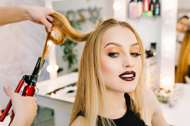 Die charmante blonde Frau des Nahaufnahmeporträts bereitet sich auf Feier, Party im Schönheitssalon vor. Stilvolles Make-up, Frisur, rote Lippen, Luxus-Look, Zufriedenheit, modisches Modell