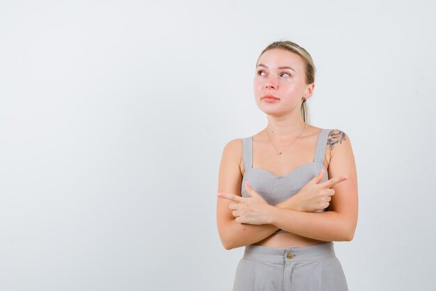 Die denkende Frau zeigt seitwärts, indem sie ihre Arme auf weißem Hintergrund verschränkt