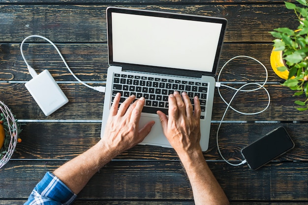 Die Draufsicht der Hand des Mannes, die auf Laptop schreibt, schloss an Energiebank und Mobiltelefon an