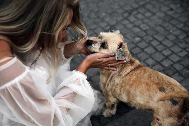 Die Frau, die in das schöne weiße Kleid gekleidet ist, schaut den niedlichen Hund an