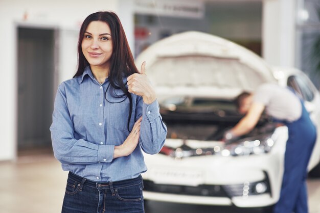 Die Frau genehmigt die Arbeit des Kunden. Der Mechaniker arbeitet unter der Motorhaube des Autos