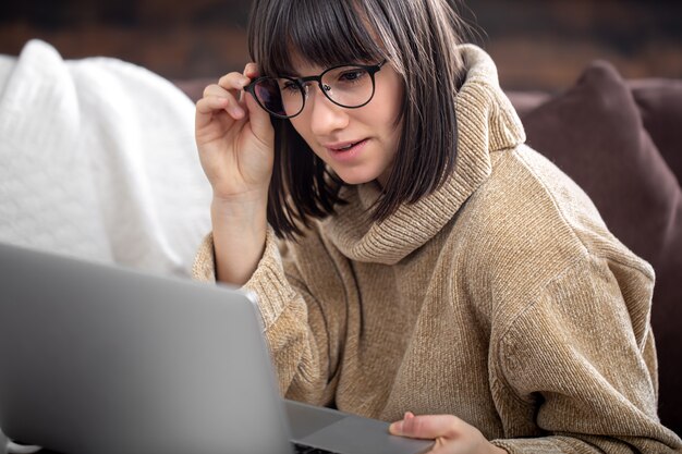 Die Frau mit der Brille schaut konzentriert auf den Laptop-Bildschirm. Das Konzept der Fernarbeit, freiberuflich tätig.