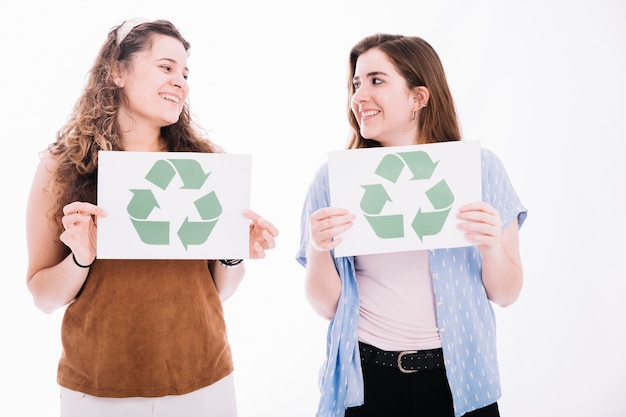 Die Frauen, die einander betrachten, halten Recyclingikonenplakat auf weißem Hintergrund auf