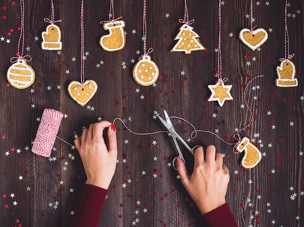 Die Frauenhand, die Scheren hält, bereitet Lebkuchen für das Hängen am Weihnachtsbaum zu