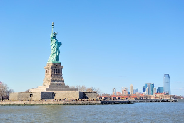 Die Freiheitsstatue steht vor der Skyline von New York City Manhattan mit Wolkenkratzern über dem Hudson River mit klarem blauem Himmel.