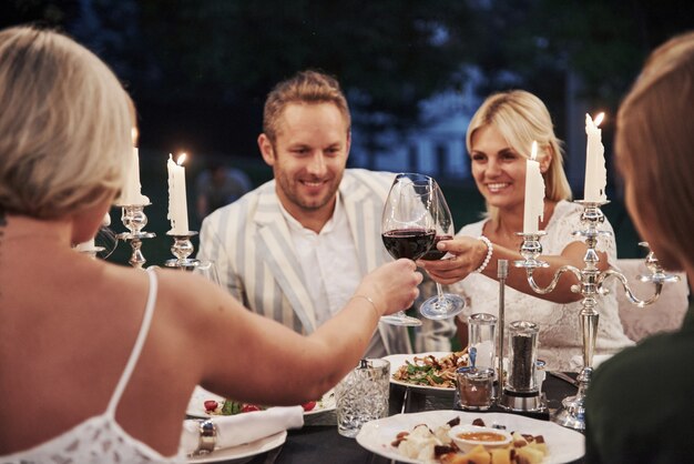 Die Gläser mit Wein klopfen. Eine Gruppe von Freunden in eleganter Kleidung hat ein luxuriöses Abendessen