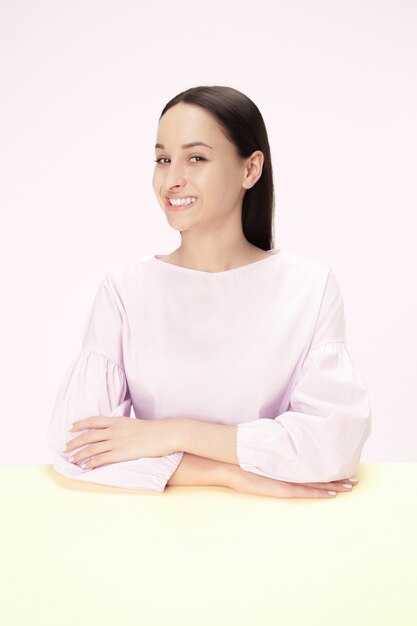 Die glückliche und lächelnde Geschäftsfrau, die am Tisch auf einem rosa Raum sitzt