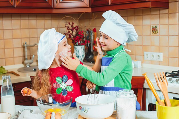 Die glücklichen zwei lustigen Kinder bereiten den Teig vor, backen Kekse in der Küche