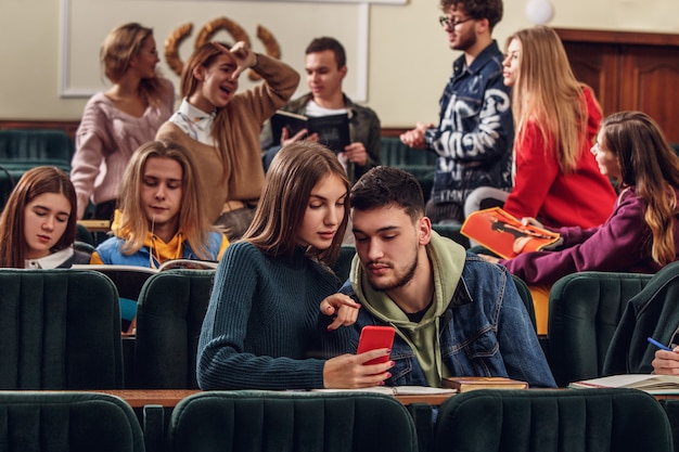 Die Gruppe fröhlicher, fröhlicher Schüler, die vor dem Unterricht in einem Hörsaal sitzen