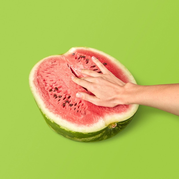 Die Hälfte der reifen Bio-Wassermelone mit den Fingern der Frau im Inneren