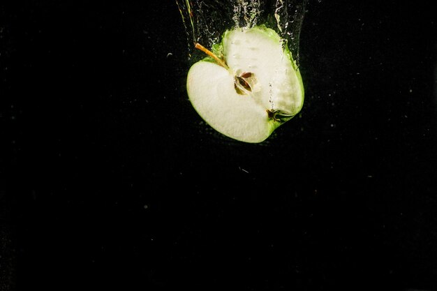 Die Hälfte des Apfels fällt in Wasser auf schwarzem Hintergrund
