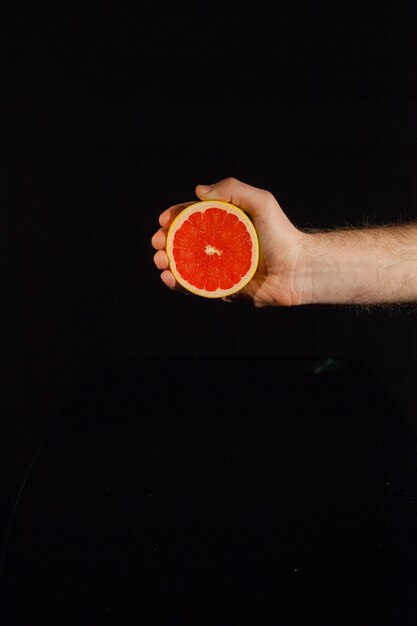 Die Hälfte einer saftigen Grapefruit in der Hand des Mannes auf schwarzem Hintergrund