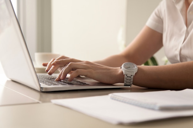 Die Hände der Frau, die auf Laptop am Arbeitsplatz schreiben