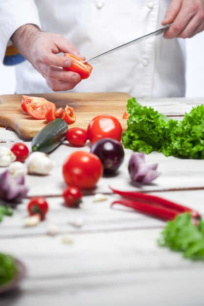 Die Hände des Küchenchefs schneiden eine rote Tomate in seiner Küche auf weißem Hintergrund mit leerem Rohling für das Rezept