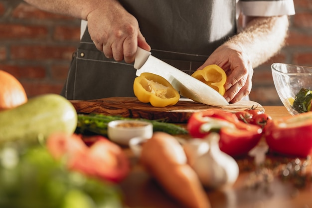 Die Hände des Küchenchefs schneiden Gemüse in seiner Küche