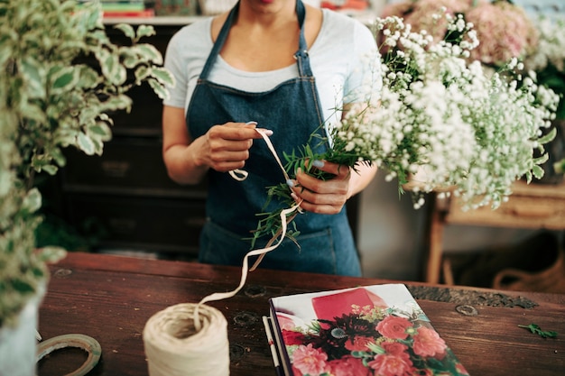 Die Hand der Frau, die Blumenstrauß mit Schnur im Shop bindet