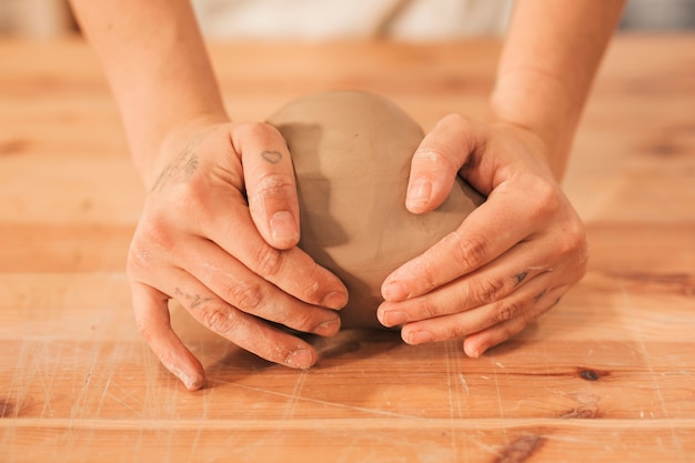 Die Hand der Frau, die den Lehm auf Holztisch knetet