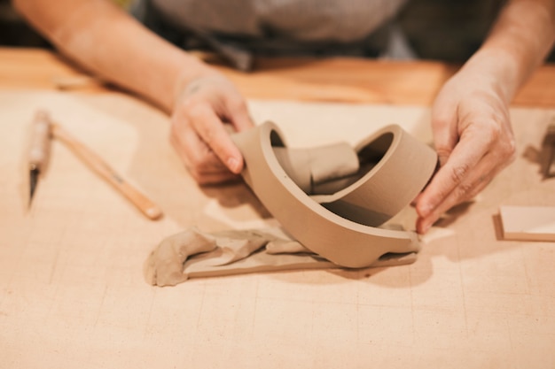 Die Hand der Frau, die kreatives Produkt mit Lehm auf hölzernem Schreibtisch macht