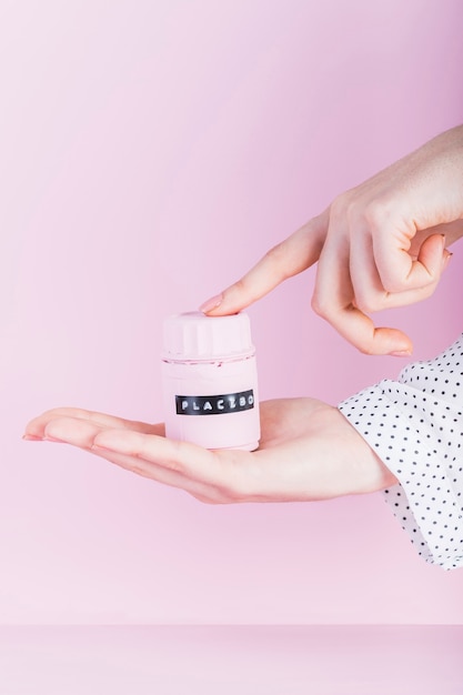 Kostenloses Foto die hand der frau, die placeboflasche über rosa hintergrund hält