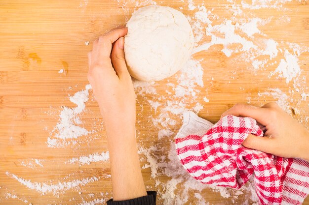 Die Hand der Frau, die Teig auf hölzernem Schreibtisch vorbereitet