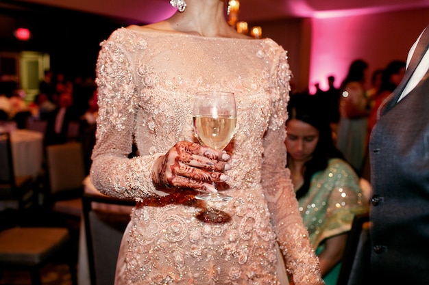 Die Hand der indischen Frau, die mit mehndi gemalt wird, hält ein Glas Wein