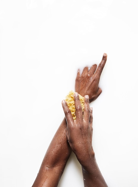 Die Hand der schwarzen Frau in einem Milchbad mit einem gelben Schwamm