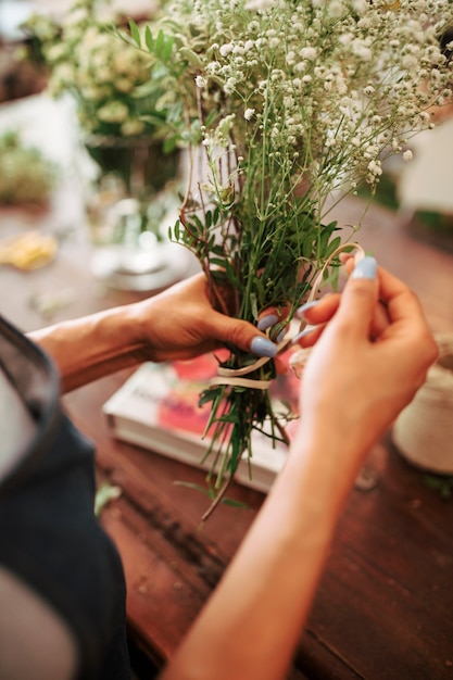 Die Hand des Floristen, die Bündel weiße Blumen mit Schnur bindet