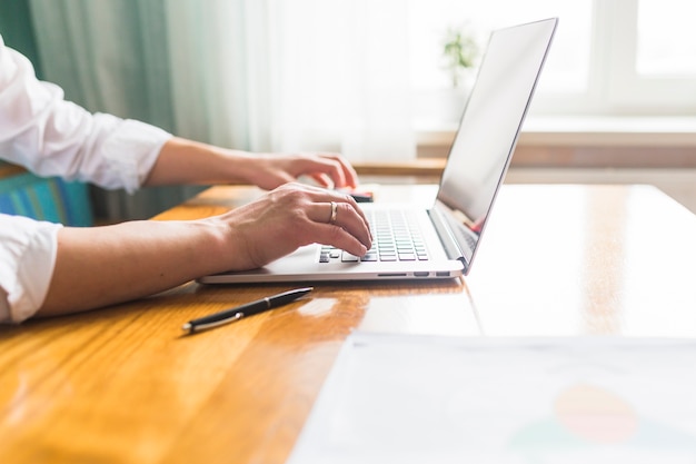 Die Hand des Geschäftsmannes, die Laptop über hölzernem Schreibtisch verwendet