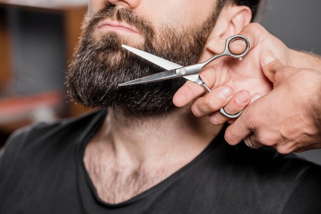 Die Hand des Herrenschnitts, die den Bart des Mannes mit Scheren schneidet