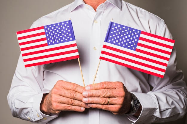 Die Hand des Mannes, die in der Hand USA-Flaggen gegen farbigen Hintergrund hält