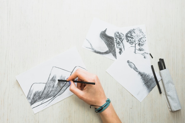 Die Hand des Menschen, die auf Papier mit Holzkohlenstock nahe schöner Hand gezeichneter Zeichnung skizziert