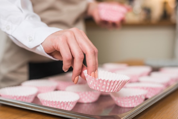 Die Hand des weiblichen Bäckers, die den Kasten des kleinen Kuchens auf das Fach setzt