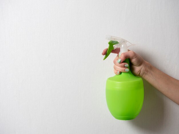 Die hand einer frau hält eine plastikflasche mit einer grünen sprühflasche auf grauem hintergrund. das konzept der häuslichen pflege und reinigung. platz kopieren
