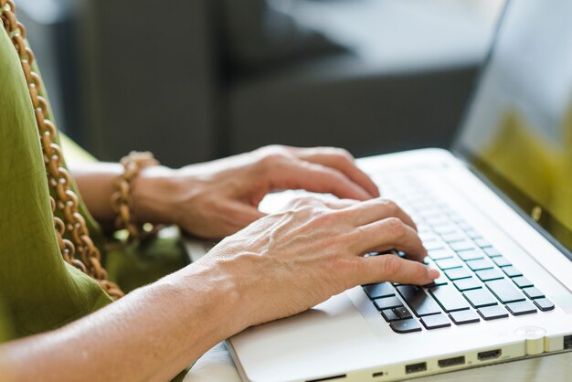 Die Hand einer gealterten Frau, die auf Laptop schreibt