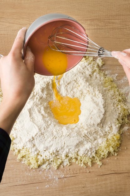 Kostenloses Foto die hand einer person, die die geschlagenen eier in das mehl und in den geriebenen käse für das zubereiten des italienischen gnocchi auf hölzernem schreibtisch gießt