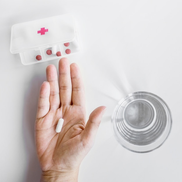 Die Hand einer Person, die Tablette vom Pillenorganisationskasten auf weißem Hintergrund nimmt